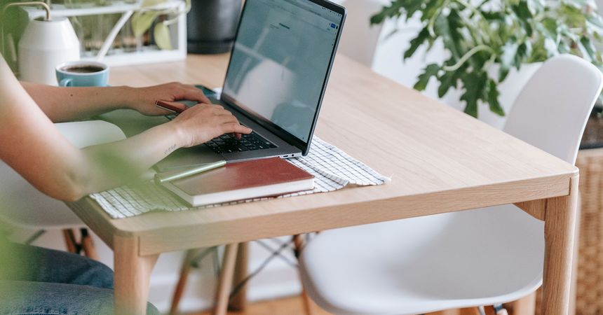 Mujer escribe en un computador en una habitación de su hogar adornada con plantas de interior.